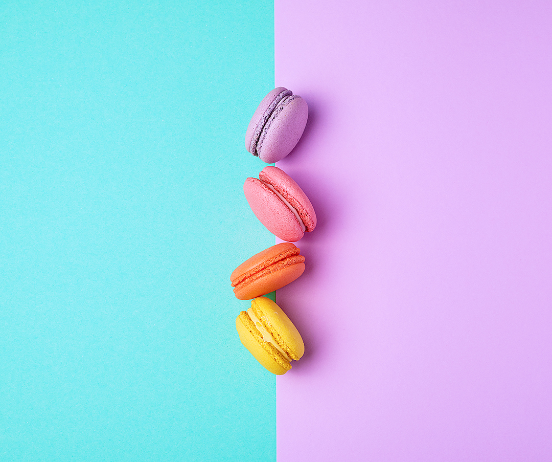 multi-colored macarons with cream on a purple-green background, flat lay, copy space